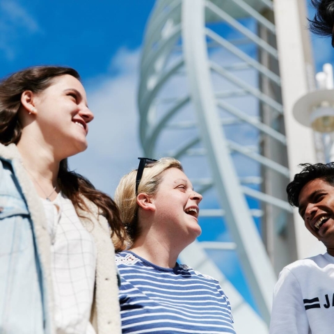 A group of people laughing together, stood against a blue sky and the Spinnaker Tower