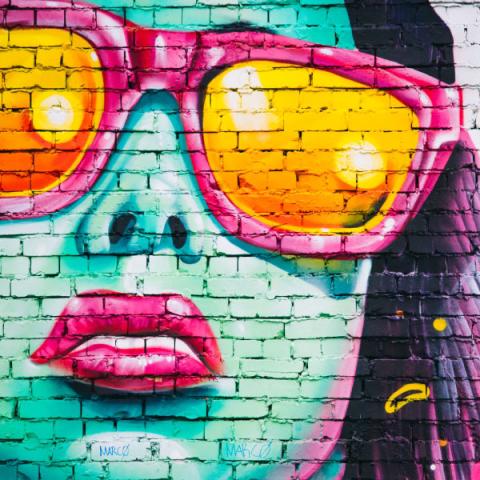 A vibrant graffiti face with oversized sunglasses on a brick wall