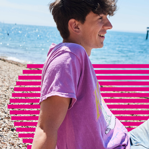 Student sat on the beach in a pink t-shirt on a sunny day
