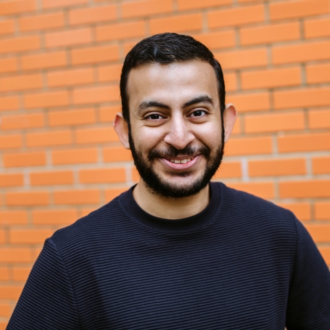 Headshot of male student stood in front of orange brick wall