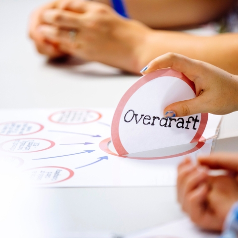 A hand holding an 'Overdraft' popup sign from a diagram on a desk