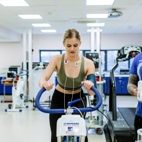 Student on bike machine with a trainer and hooked up to monitors