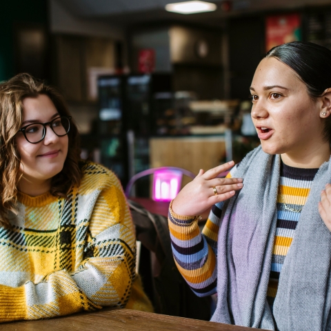 Two students sat talking to each other at a cafe