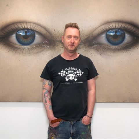 Paul Stone standing in front of his artwork smiling to camera wearing black tshirt