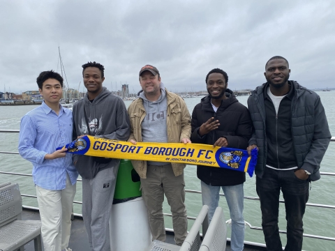 Five individuals standing on a boat, posing with a banner visible.