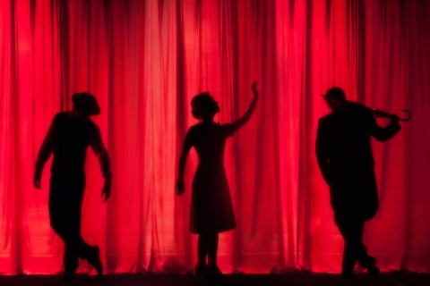 Three figures dancing in front of a red curtain