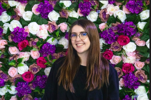 Creative Writing and Film Industries graduate, Mollie Winter, smiling in front of a colourful flower wall.