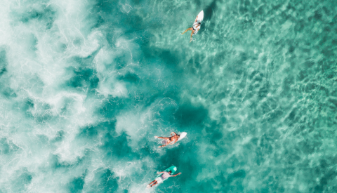 Birds-eye view of group of surfers in the ocean - Photo by Sam Wermut on Unsplash