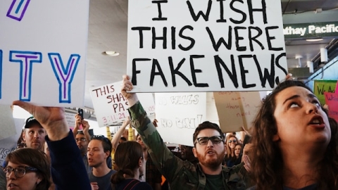 Man holding up a sign saying 'I wish this were fake news'