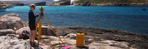 Researcher using a theodolite on the coast in Malta