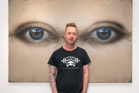 Paul Stone standing in front of his artwork smiling to camera wearing black tshirt