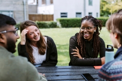 Students smiling in sun at picnic table outside of the Students' Union
