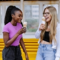 Two female students eating ice creams standing in front of a bright yellow bench at the beach